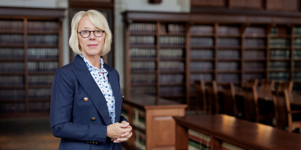 photo of Stefanie Lindquist in a blue suit and light shirt standing in front of bookshelves in a library setting