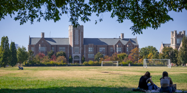 Photo of Seigle Hall during the day with two students in the bottom right corner sitting on the grass