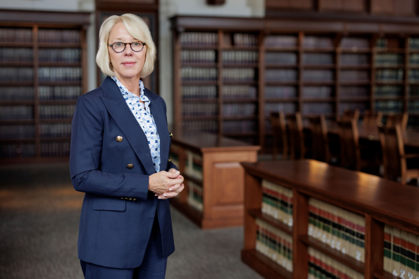 photo of Stefanie Lindquist in a blue suit and light shirt standing in front of bookshelves in a library setting