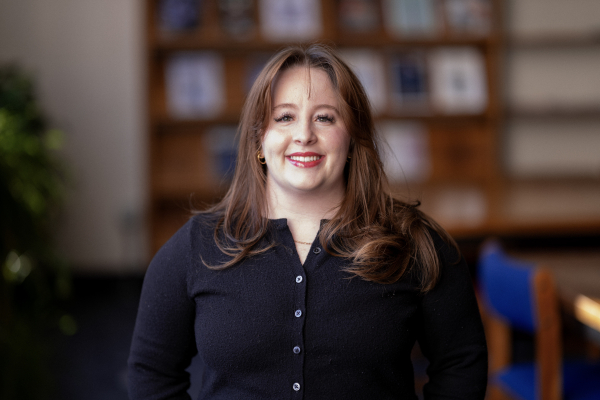 Photo of Lizzy Kearns in a library, smiling, in a black button-up top