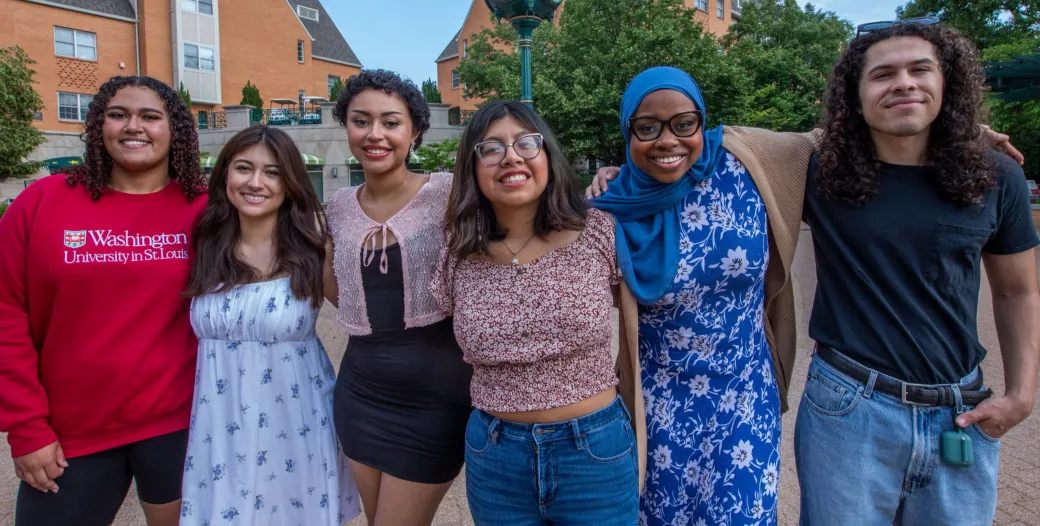 Six students of different cultural backgrounds standing and smiling with their arms around each others' shoulders.