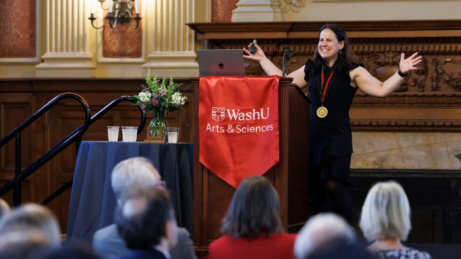Photo of Betsy Sinclair with arms raised giving a speech in front of an audience