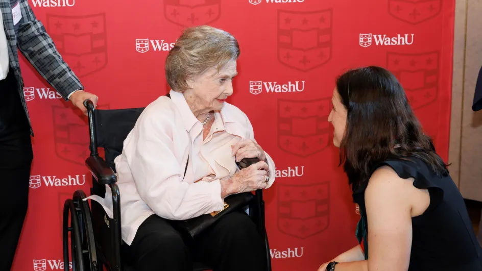 Photo of Betsy Sinclair and Barbara Ann Smith in discussion in front of a red WashU background