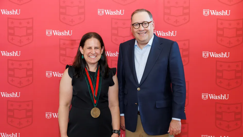 Photo of Betsy Sinclair and Chancellor Andrew Martin smiling to camera in front of a red WashU background