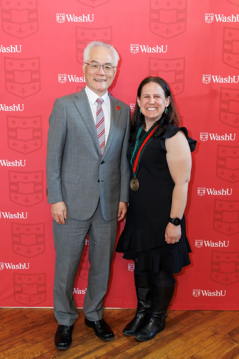 Photo of Betsy Sinclair and Dean Feng Sheng Hu smiling to camera in front of a red WashU background
