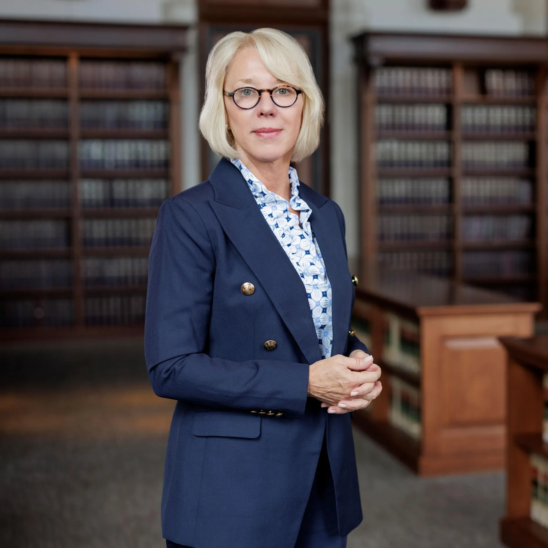 Photo of Law Dean Stephanie Lindquist looking at camera in a library wearing a blue blazer and blue patterned button up shirt