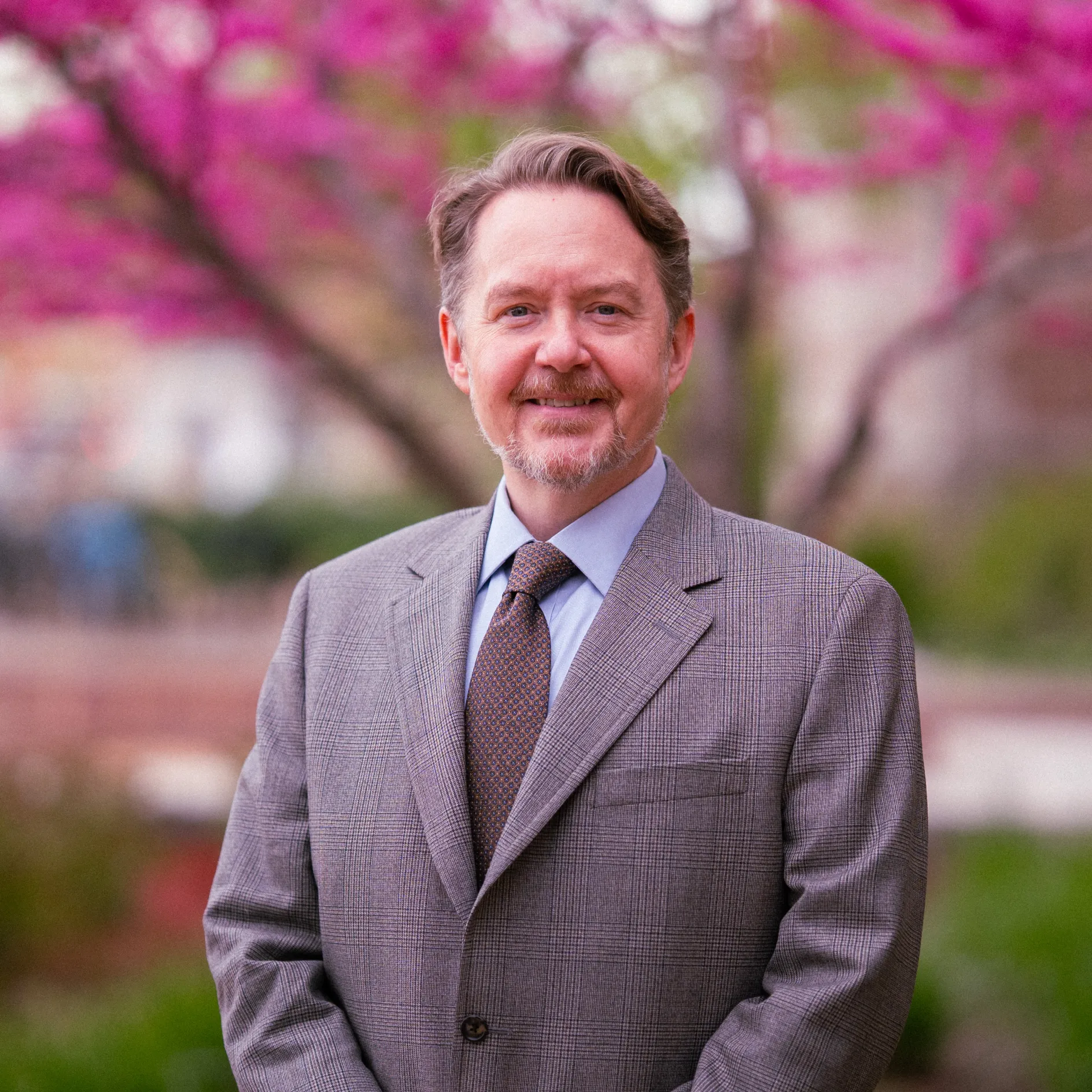 Photo of Andrew Reeves smiling to camera in a light colored blazer, tie, and button-up shirt