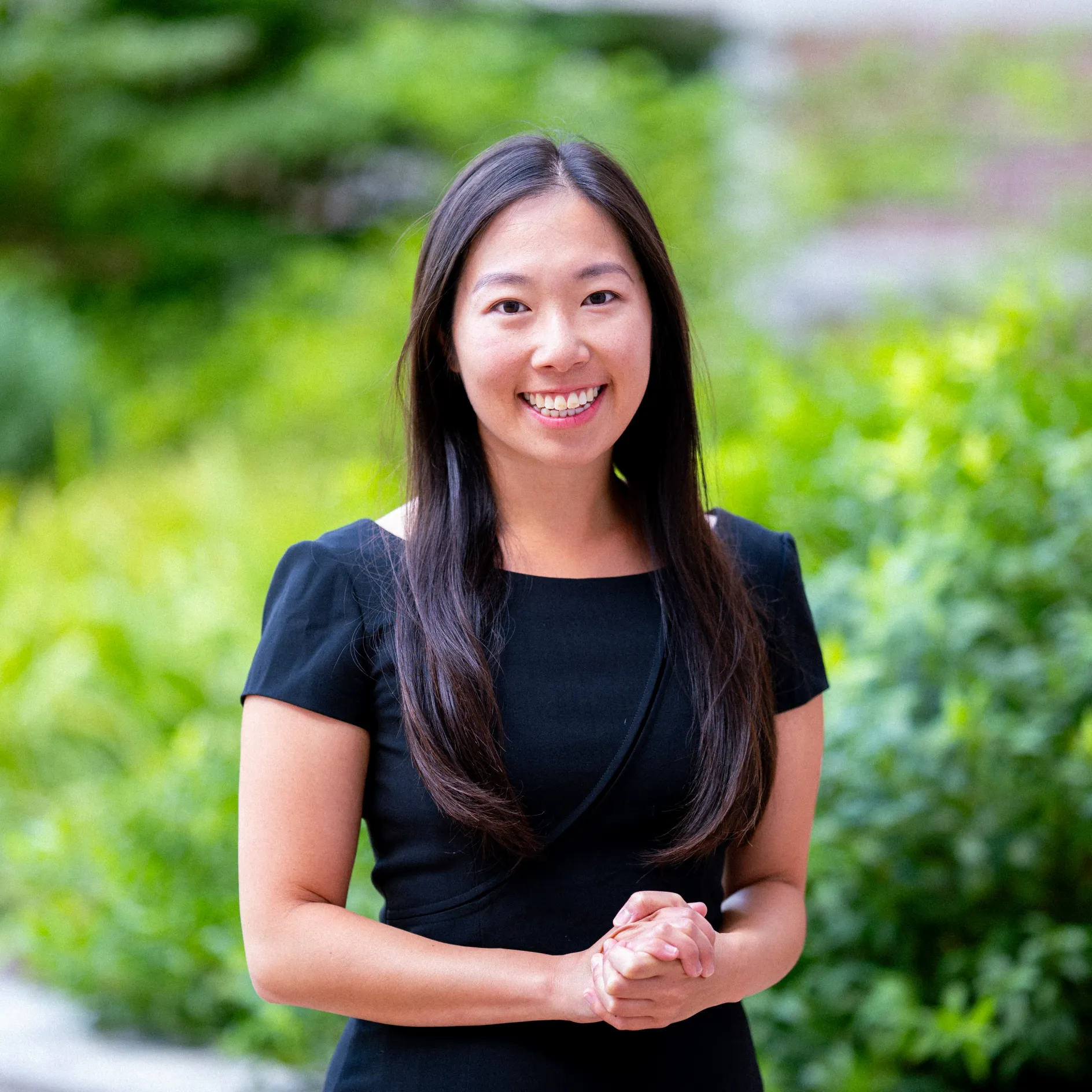 Photo of Elaine Yao smiling to the camera in front of greenery with hands clasped in front