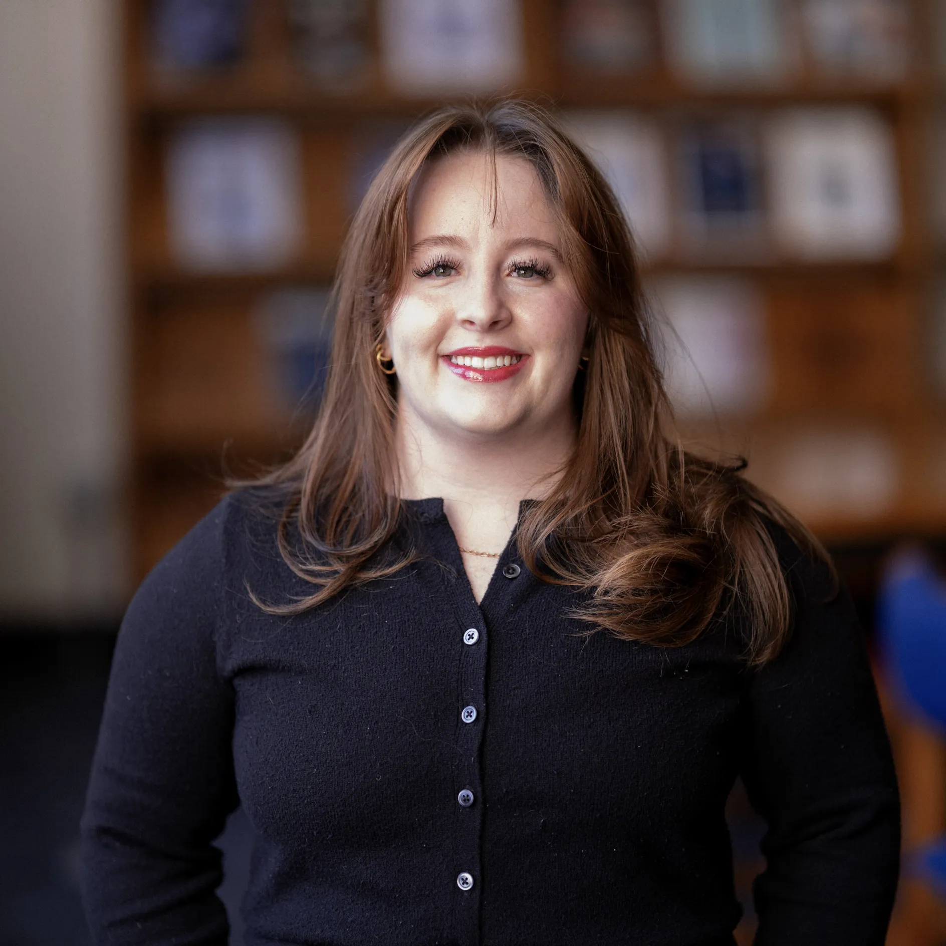 Photo of Lizzy Kearns in a library, smiling, in a black button-up top