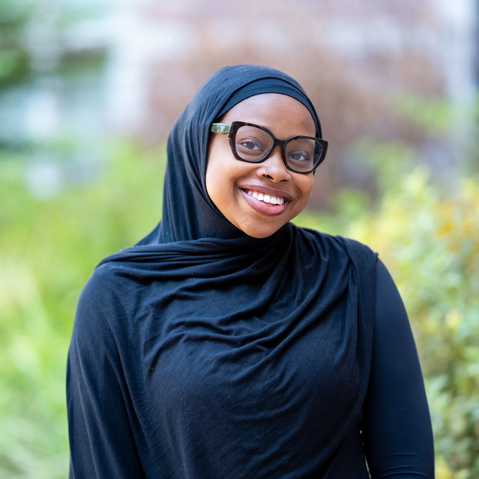 Photo of Maryam Oyebamiji smiling in glasses wearing a black head scarf