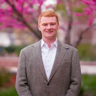 Photo of Lukas Alexander smiling to camera in a tan blazer and white button up shirt