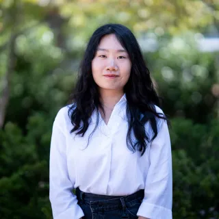 Photo of Yue Wu smiling to camera. She has long black hair and is wearing a white button up shirt